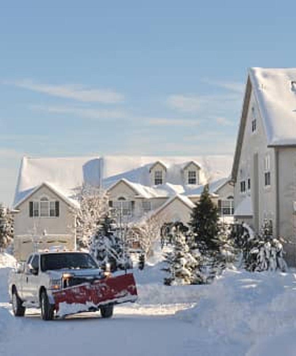 Professional snow plow truck clearing a residential driveway during winter weather.