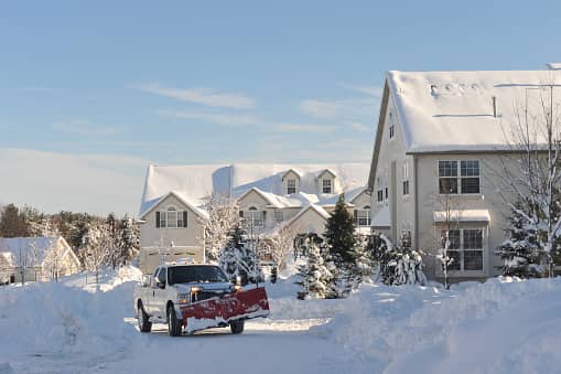 A truck with a snow plow attachment clearing a road on a snowy day.