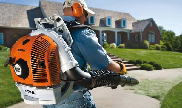 A man operating a backpack leaf blower in front of a large, well-maintained home.