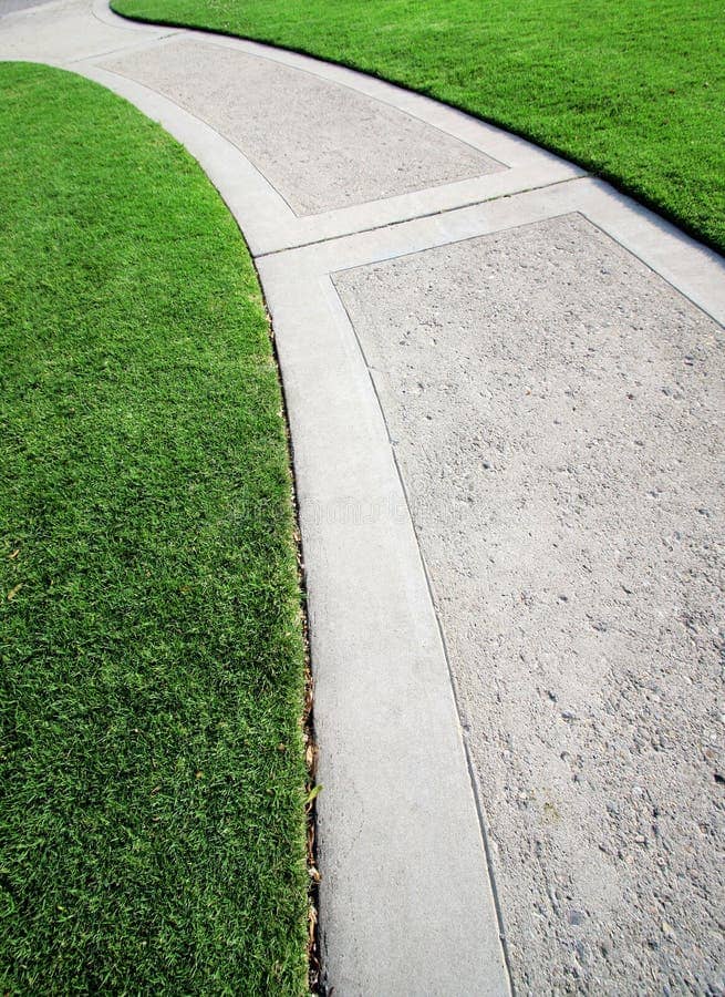 A concrete walkway with excellent edging through a field of green grass.