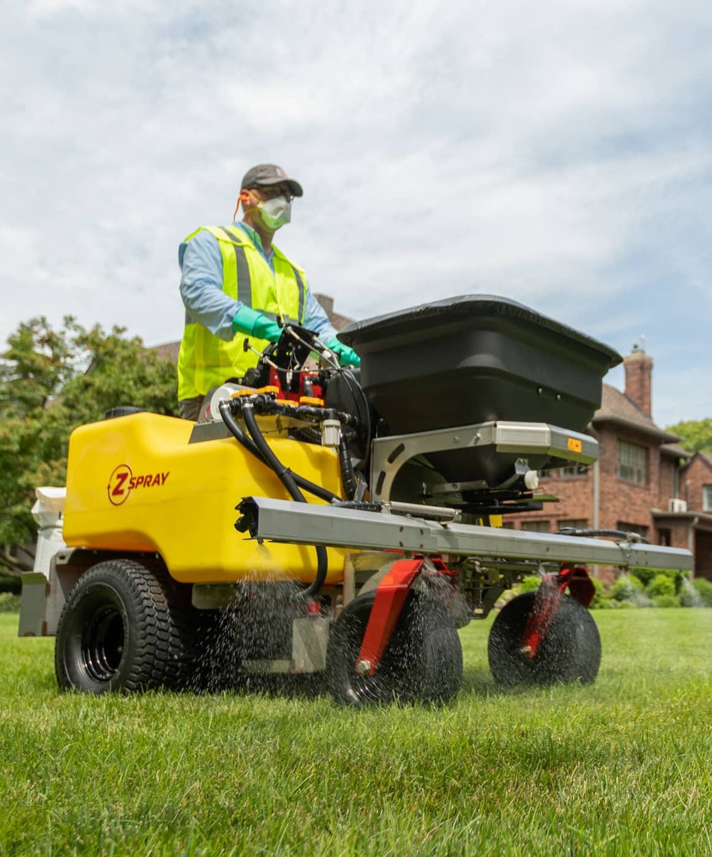 Professional lawn care technician using commercial spray equipment to apply fertilizer treatments evenly across a residential lawn.